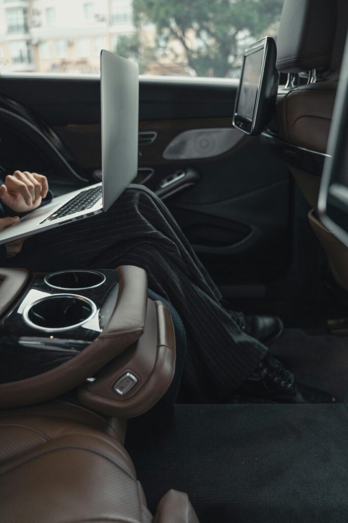 An image showing a person sitting in the back of a car on a laptop
