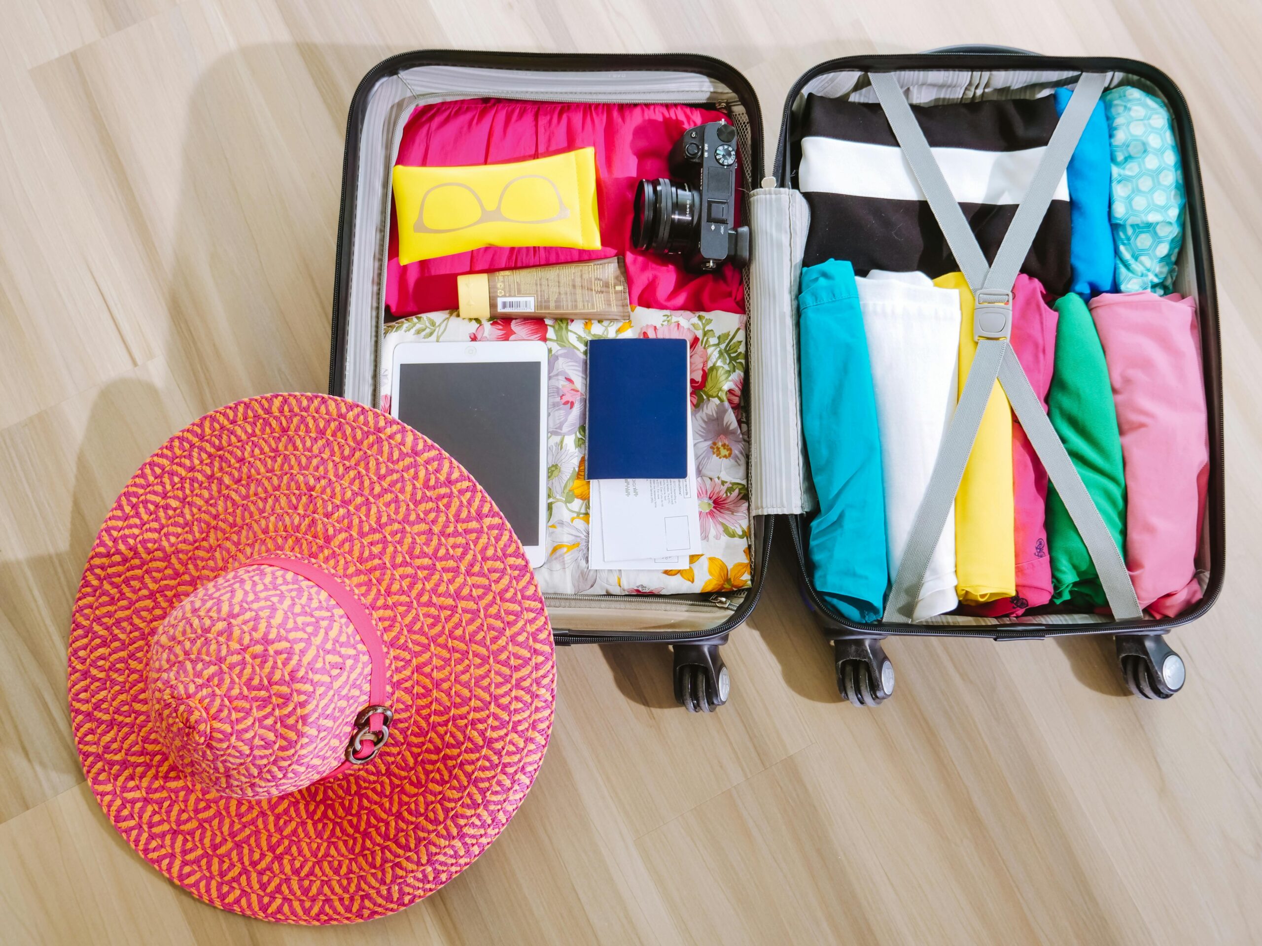 An image showing an open packed suitcase next to a sun hat